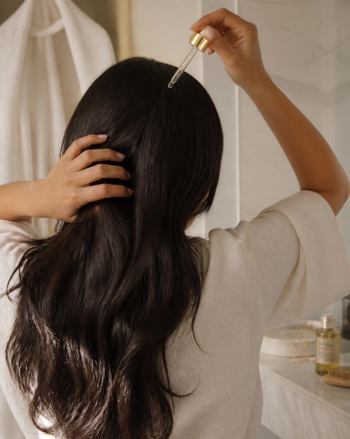 Femme appliquant l'huile capillaire NOOR sur son cuir chevelu